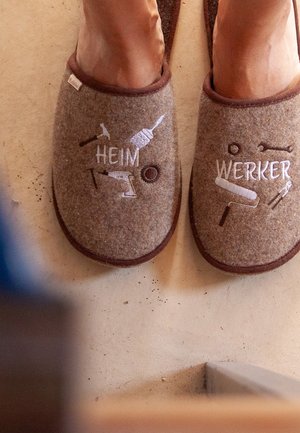 Brown felt slippers with embroidered tools and the words "HEIM" and "WERKER" on each slipper, featuring a textured surface and brown trim.