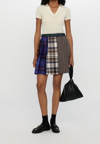 Minifalda a cuadros con varios patrones de tartán en azul, marrón y blanco, con una cinturilla negra sólida; combinada con una blusa ajustada color crema.
