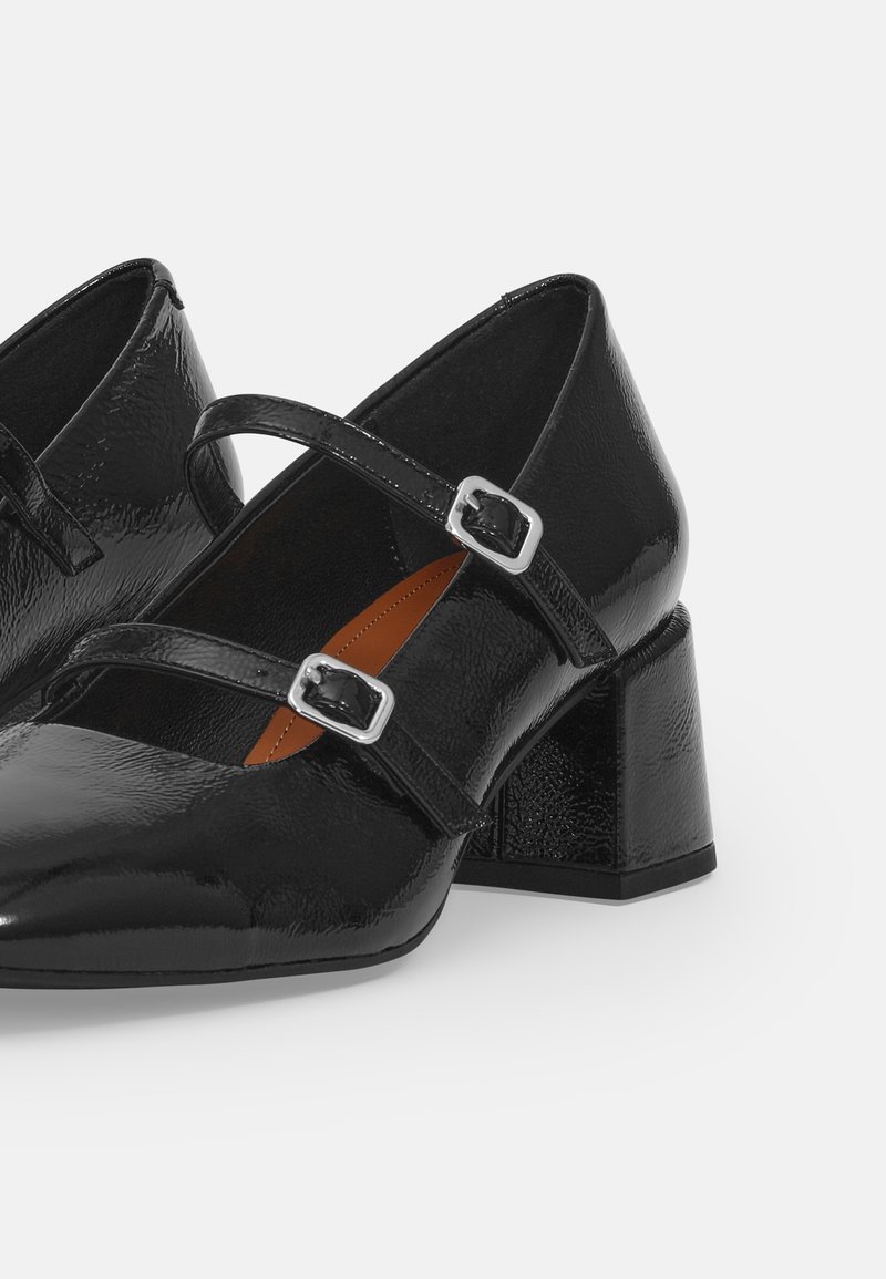 Zwarte lakleren schoenen met blokhak, voorzien van twee verstelbare banden met vierkante gespen. Heeft een puntige neus en een gestructureerd oppervlak.