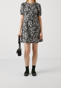 Černé šaty s krátkými rukávy a bílým vzorem růží, přiléhavý korzet, rozšířená sukně, doplněno černými botami, zelenými ponožkami a malou černou kabelkou.