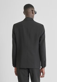 Blazer negro a medida con un diseño estructurado, que presenta una textura suave, cuello con muesca y puños con botones. Vista trasera mostrada.