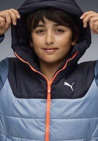 Marineblau und hellblauer Daunenjacke mit einem orangefarbenen Reißverschluss, ausgestattet mit einer Kapuze und einem weißen Puma-Logo im Brustbereich.