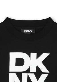 Schwarzes Baumwoll-T-Shirt mit geripptem Rundhalsausschnitt. Mit großem weißen "DKNY"-Logo, das in fetten, Großbuchstaben auf der Vorderseite gedruckt ist.