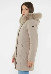 Beżowa parka z kapturem, z futrzanym wykończeniem, kieszeniami na suwak i prostym krojem. Gładka tekstura materiału, zaprojektowana dla ciepła.