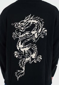 Czarny sweter dzianinowy z białym wzorem smoka na plecach, prezentujący skomplikowane detale i teksturowany materiał.