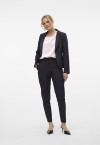 Svart skreddersydd blazer over en lys rosa bluse, kombinert med slanke svarte bukser og svarte høye hæler. Fokus på tettsittende silhuett.