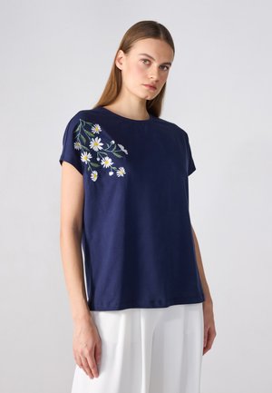Navy sininen puuvillapaita, lyhyet hihat, vasemman olkapään valkoista ja keltaista päivänkakkara-embroideryä, rento malli.