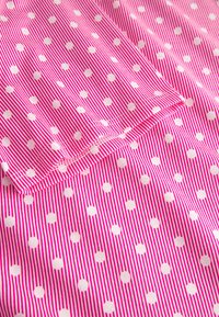 Bomuldsstof med lyserødt og hvidt stribet mønster med skiftende hvide prikker, der viser en glat tekstur og lige syningsdetaljer.