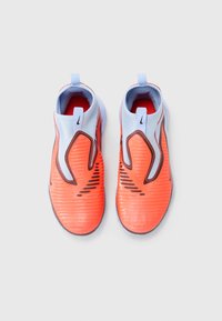 Jasne oranžové a biele Nike športové tieňovky s čiernymi detailmi, pohľad zhora na jednoduchom svetlo šedom pozadí.