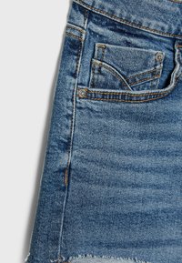 Falda de mezclilla, lavado azul claro, dobladillo desflecado, diseño tradicional de cinco bolsillos, costuras visibles en dorado y azul, tela texturizada.