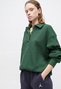 Suéter verde con canalé y cuello con solapa, con una fila de botones. Combina con pantalones de chándal azul marino, que presentan el logo de Jordan.