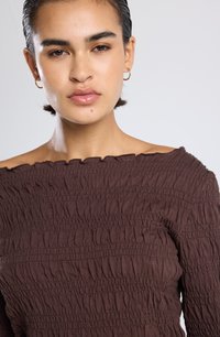 Top marrón, con los hombros al descubierto, que presenta un smocking texturizado, con bordes rizados y una silueta ajustada. Tejido de algodón suave con detalles fruncidos.