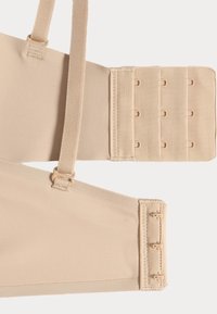 Beige verstelbaar compressiekledingstuk met elastische banden, haak-en-oogsluitingen, een gladde textuur en versterkte stikseldetails.