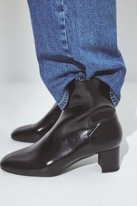 Črne, sijoče gležnjarje s koničastim nosom in nizko blokasto peto, oblečene z modrimi jeans hlačami, ki prikazuje gladko teksturo in eleganten dizajn.