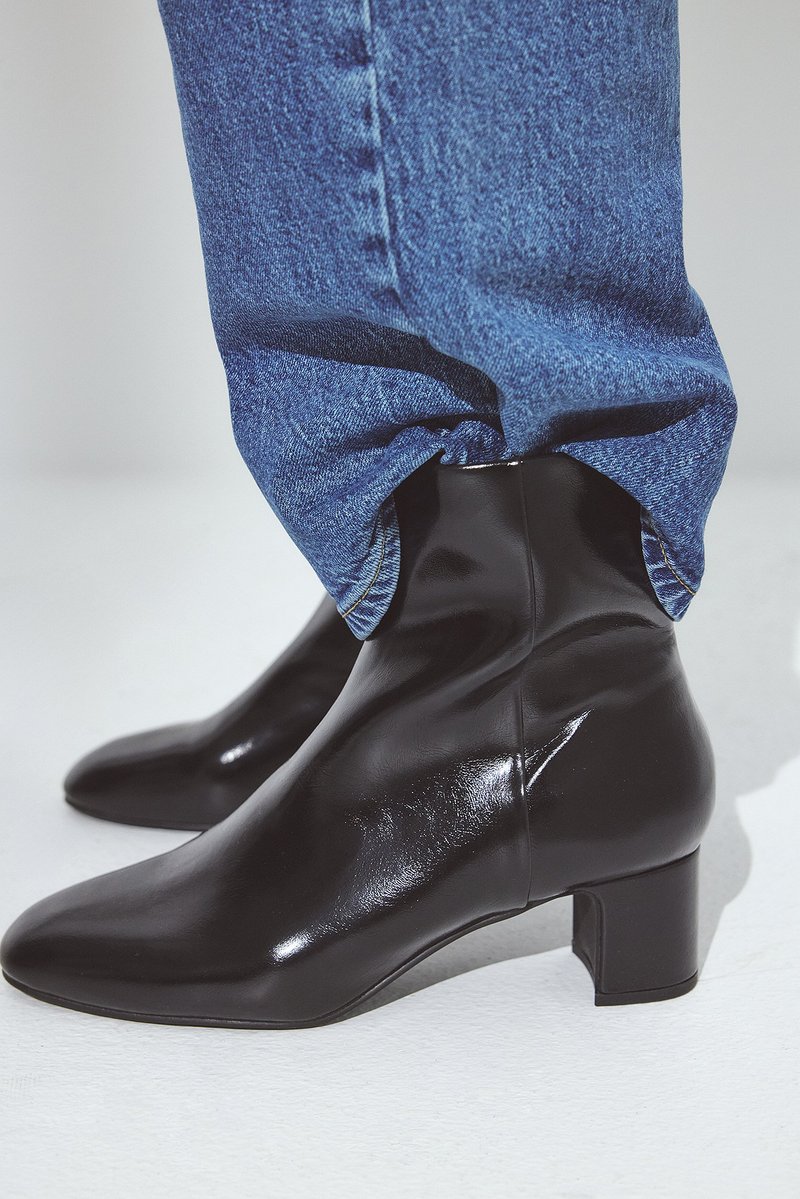 Črne, sijoče gležnjarje s koničastim nosom in nizko blokasto peto, oblečene z modrimi jeans hlačami, ki prikazuje gladko teksturo in eleganten dizajn.