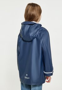 Tamsiai mėlynas vandeniui atsparus lietpaltis su kapišonu, turintis blizgų paviršių ir baltas akcentines juosteles ant rankovių. Logotipas atspausdintas netoli apvado.