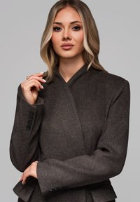 Brun, tekstureret jakke med omslagsdesign, der har krave og knapdetaljer på ærmerne. Velegnet til formel eller forretningsattire.