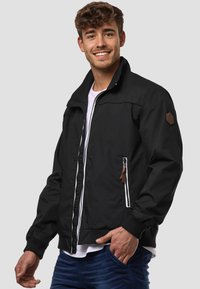Black jacket with a high collar, zippered front, and two side pockets. Features a brown leather logo patch on the left shoulder.