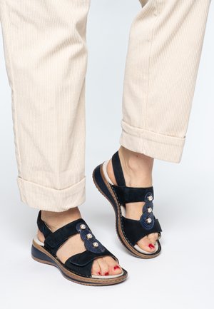 Navy suede sandals with an open toe, dual straps, and decorative buttons. Features a textured sole and cushioned footbed.
