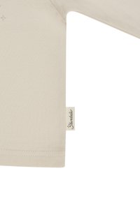 Light beige long-sleeve shirt made of soft cotton. Features a stitched hem and labeled tag with "Skentsdale" logo on the side seam.