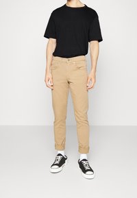 T-shirt nera a maniche corte, pantaloni slim fit khaki, calzini bianchi e sneakers nere con suola bianca. Design semplice con colori classici.