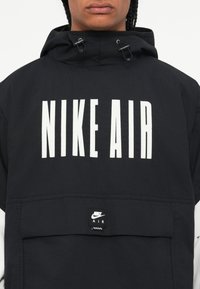 Juodas Nike džemperis su dideliu baltu "NIKE AIR" spaudiniu per krūtinę, su priekinėmis kišenėmis ir reguliuojamu gaubtu.