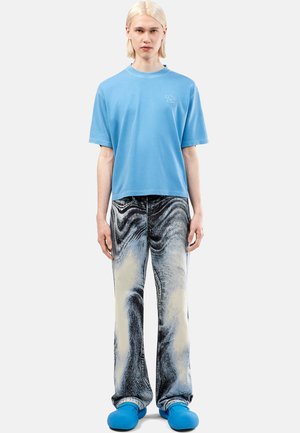Lichtblauw katoenen T-shirt met korte mouwen, gecombineerd met zwart en crèmekleurige gemarmerde jeans. Blauwe instapschoenen maken de outfit compleet.