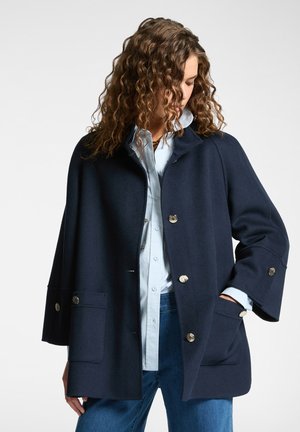 Navy wool blend coat with a relaxed shape, featuring a collar, two large front pockets, and silver-tone buttons. Smooth texture with a structured design.