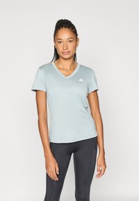 Αθλητική μπλούζα σε ανοιχτό γαλάζιο με V-λαιμόκοψη, κοντά μανίκια και διακριτικό λογότυπο Adidas στο αριστερό στήθος. Απαλή, λεία υφή υφάσματος.