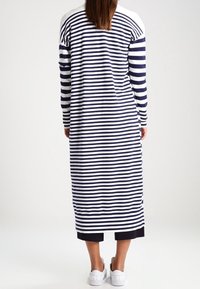 Pruhované šaty s horizontálními námořnickými a bílými pruhy, dlouhými rukávy a volným střihem, doplněné bílými teniskami.