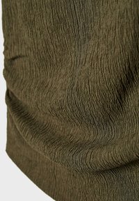 Primo piano di tessuto verde oliva con superficie strutturata e increspata e pieghe morbide che creano ombre sottili.