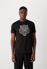 Zwart T-shirt met korte mouwen, met een grafisch ontwerp van een witte tijgerkop in het midden, gemaakt van katoen met een zachte textuur.