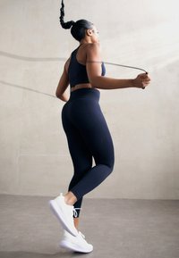 Crni atletski crop top i tajice, upareni s bijelim tenisicama, imaju glatku teksturu i uski kroj, idealni za vježbanje.