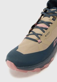 Beige and navy trail shoe with textured upper, lace-up design, and pink accents; features GORE-TEX branding and a durable rubber sole.
