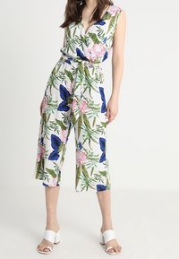Mono floral con escote en V profundo, mangas cortas, cintura ajustada y piernas cortas. Tela blanca con mariposas azules y flores rosas.