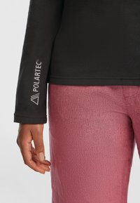 Zwarte fleece sweatshirt met een gestructureerd oppervlak, voorzien van een wit Polartec-logo op de mouw. Gecombineerd met vervaagde roze geweven broek.