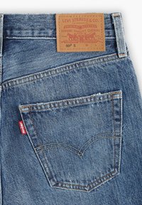 Farkut, joissa on takatasku ja punainen Levi's-tunnus. Vaaleansininen väri näkyvillä ompeleilla ja ruskea nahkaleima vyötäröllä.