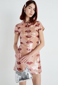 Robe courte rose avec une finition en sequins ornée de motifs de lèvres rouges, un col et une fermeture éclair à l'avant. Accompagnée d'un petit sac en sequins argentés.