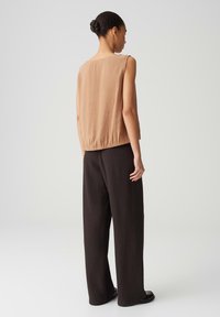 Top senza maniche color tan con orlo arricciato; abbinato a pantaloni neri larghi con pieghe e scarpe nere flat. Tessuto liscio con una vestibilità comoda.
