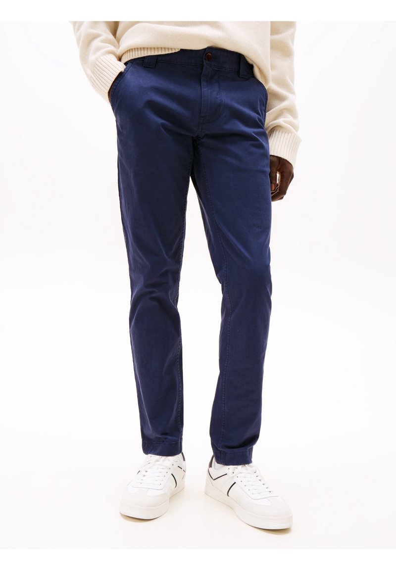 Granatowe bawełniane chinosy o prostym kroju, z przednimi kieszeniami, zapięciem na guzik i kontrastującymi przeszyciami, zestawione z białymi trampkami.