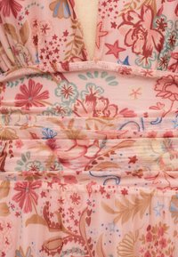 Rosa stoff med detaljerte blomster- og stjernemønstre i rødt, blått, beige og grønt, som viser samlet og rynket tekstur.