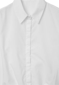 Camicia bianca con colletto a punta, caratterizzata da una texture liscia e una pattina frontale. Design semplice, senza motivi o decorazioni.