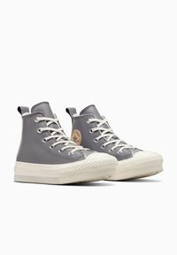 Zapatillas altas de cuero gris con suelas de goma blanca, diseño tradicional de cordones y un logo circular en el lado. Parte superior texturizada.