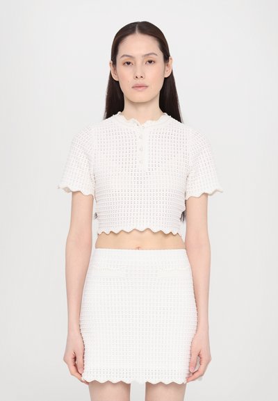 Hvid strikket cropped top med korte bølgede ærmer, struktureret mønster og knaplukning, parret med en matchende tætsiddende nederdel.