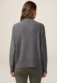 Pulover gri tricotat cu guler înalt, umeri căzuți și margine și mansete ribbed. Materialul pare moale și ușor texturat.