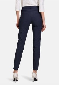 Granatowe spodnie o dopasowanym kroju wykonane z gładkiego materiału, mające dwa tylne kieszenie, zestawione z wysokimi obcasami.