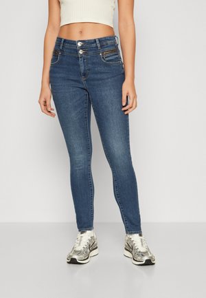 Jeans en denim skinny de couleur bleu foncé, dotés d'une taille haute avec deux boutons, d'une poche à monnaie et de détails de couture discrets. À associer avec des baskets argentées.