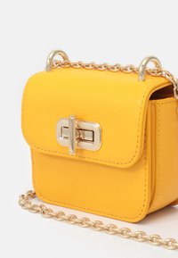 Żółta skórzana torebka o strukturalnym designie, z elementami w kolorze złota i łańcuszkowym paskiem. Posiada fakturowane zapięcie oraz starannie zszyte brzegi.