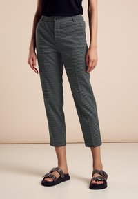 Pantaloni a quadri verdi e neri con una vestibilità slim e lunghezza cropped, abbinati a sandali neri con accenti e fibbie in argento.