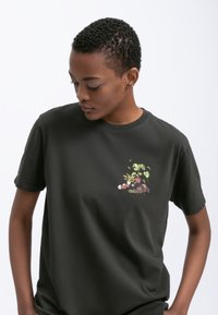 Donkergroene katoenen t-shirt met een ronde hals, met een geïllustreerd zakontwerp van planten en kleine potten in levendige kleuren.